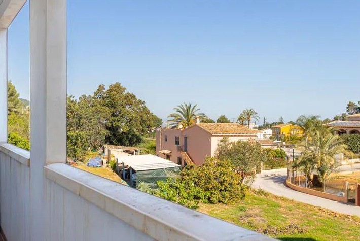 View from the balcony overlooking the village of Jesús Pobre, featuring Mediterranean architecture, palm trees, and clear blue skies over the countryside.