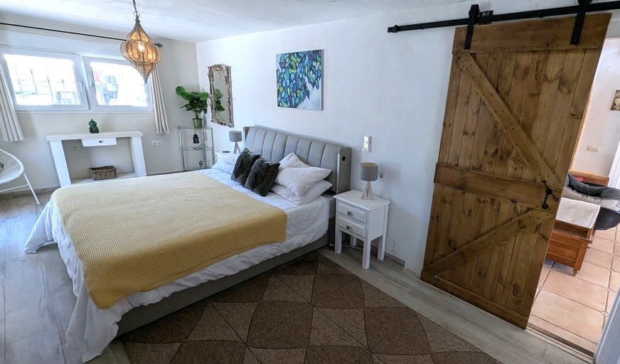 Bright bedroom featuring a rustic sliding wooden door, upholstered headboard, and a decorative Moroccan-style hanging lantern over wood-effect flooring.
