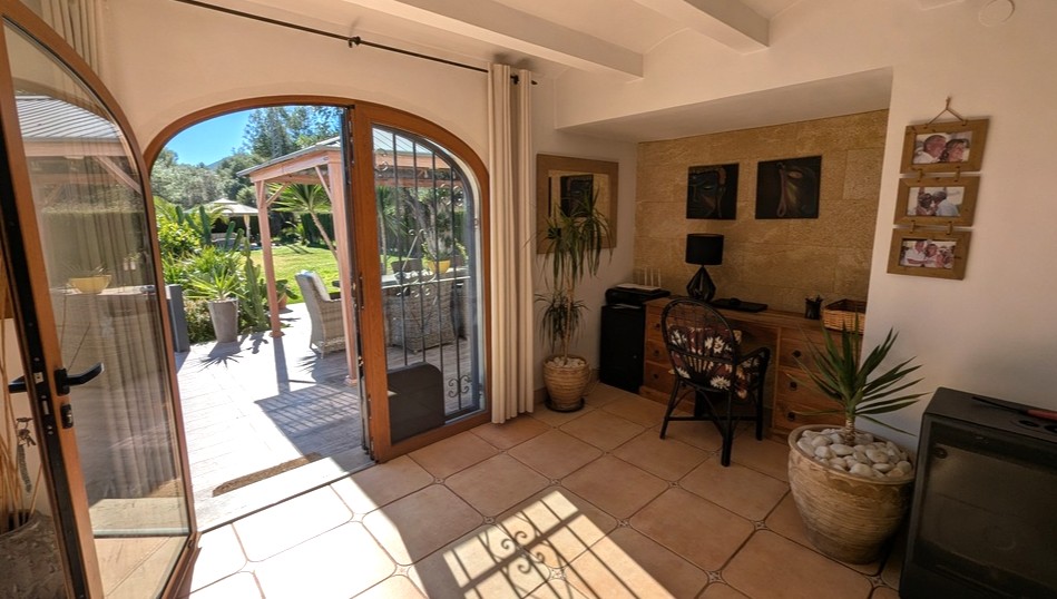 Bright interior study featuring terracotta flooring, a natural stone accent wall, and arched wooden doors opening onto a sun-drenched garden terrace.