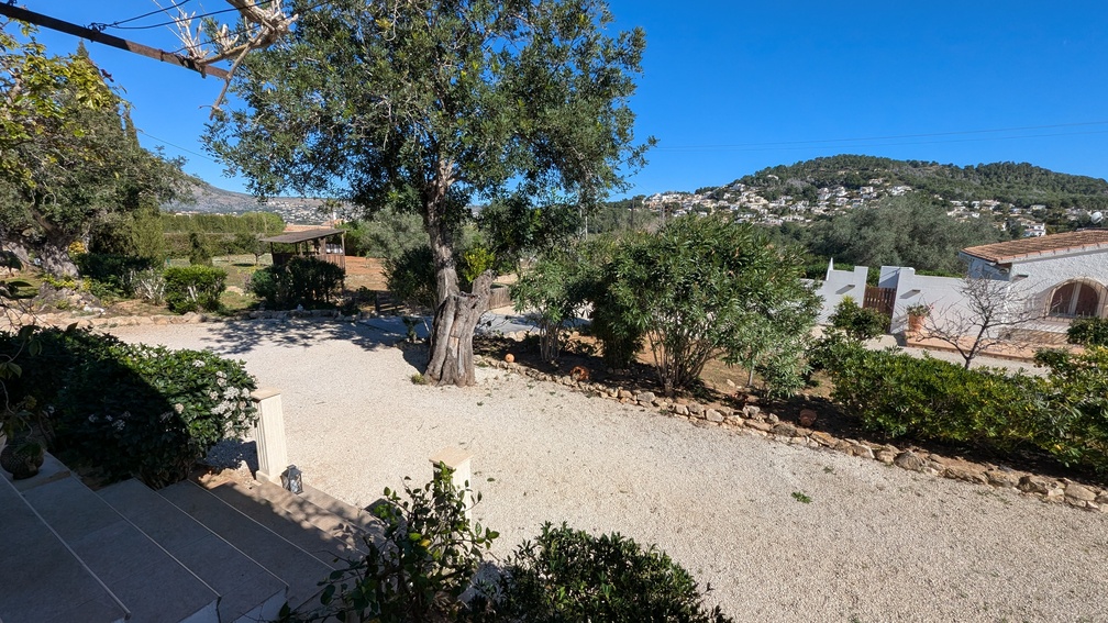 Elevated view of the gravel driveway and Mediterranean gardens, featuring mature olive trees and views toward the surrounding hillsides and residential areas of Jávea.