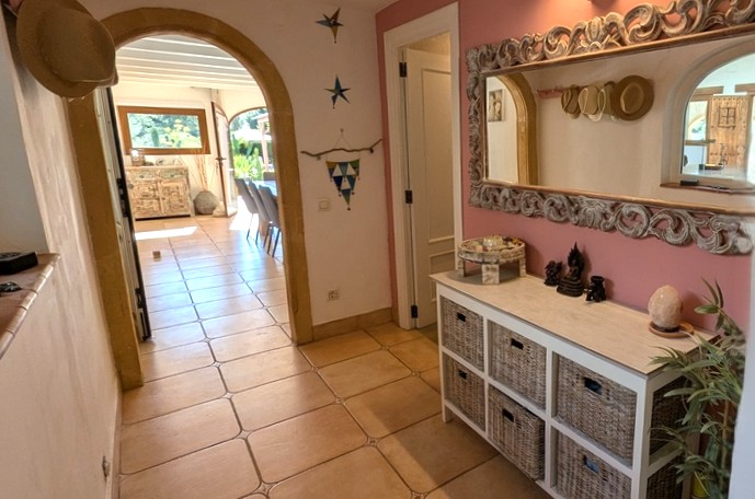Entrance hallway featuring a traditional Tosca stone arch, terracotta tiled flooring, and an ornate mirror above a sideboard with wicker storage.