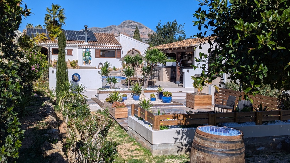 Landscaped Mediterranean garden with tiered terraces, summer kitchen, and villa with solar panels, offering clear views of the Montgó mountain.