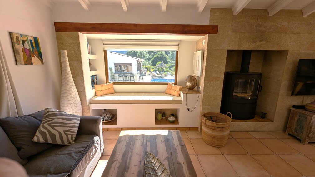 Living area featuring a built-in window seat with pool views, a modern wood-burning stove set in a Tosca stone wall, and traditional beamed ceilings.