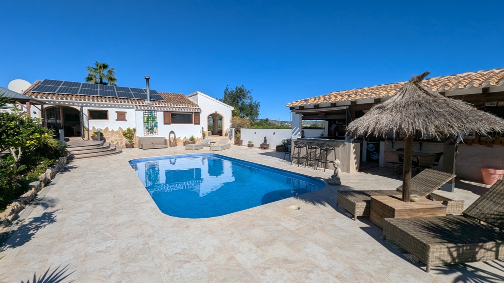 Main villa exterior featuring a private pool, stone-tiled terrace, and a fully equipped summer kitchen with bar seating, complemented by rooftop solar panels.