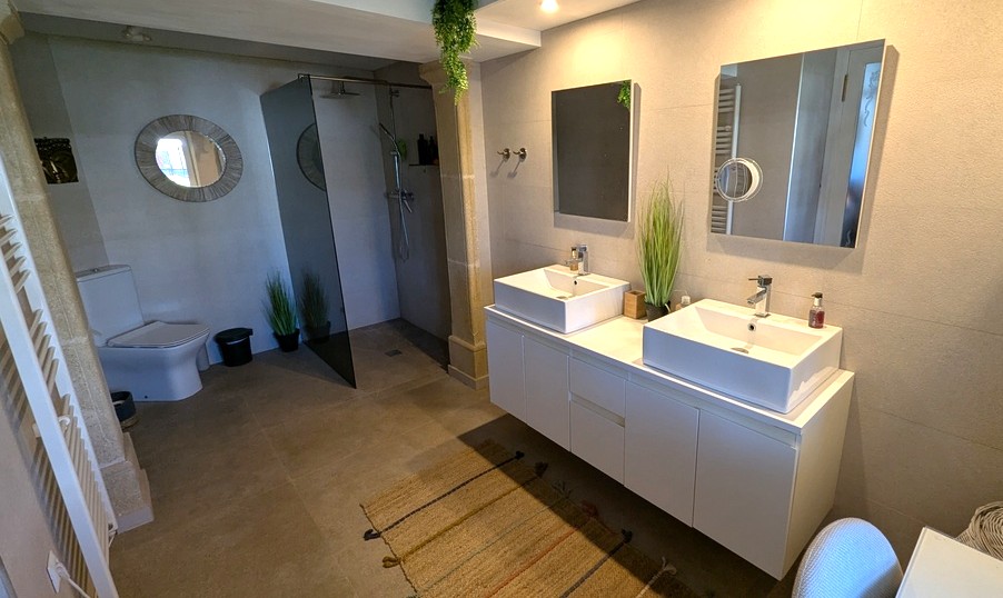 Modern bathroom featuring a double vanity with vessel sinks, a walk-in shower with a tinted glass screen, and neutral stone tiling throughout.