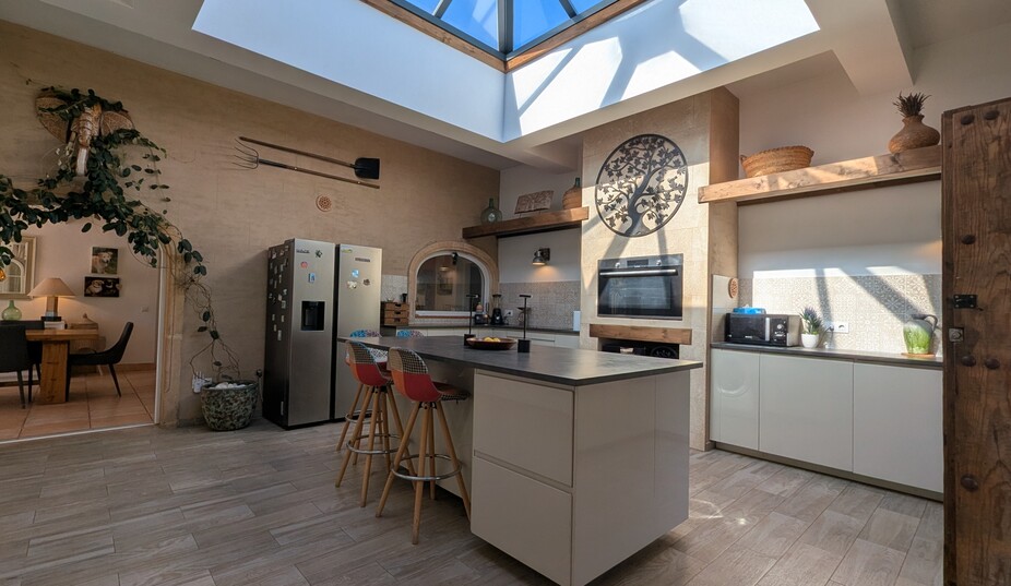 Modern kitchen featuring a large central skylight dome, a functional island with seating, and rustic stone walls decorated with traditional tools.