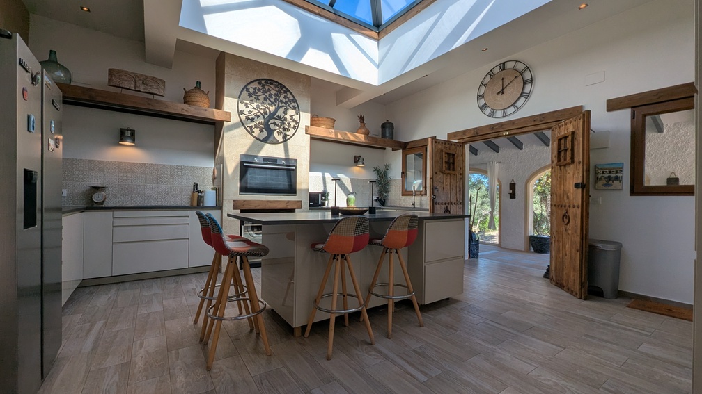Modern kitchen featuring a unique glass roof lantern, central island with seating, and traditional wooden doors leading to the adjacent naya.
