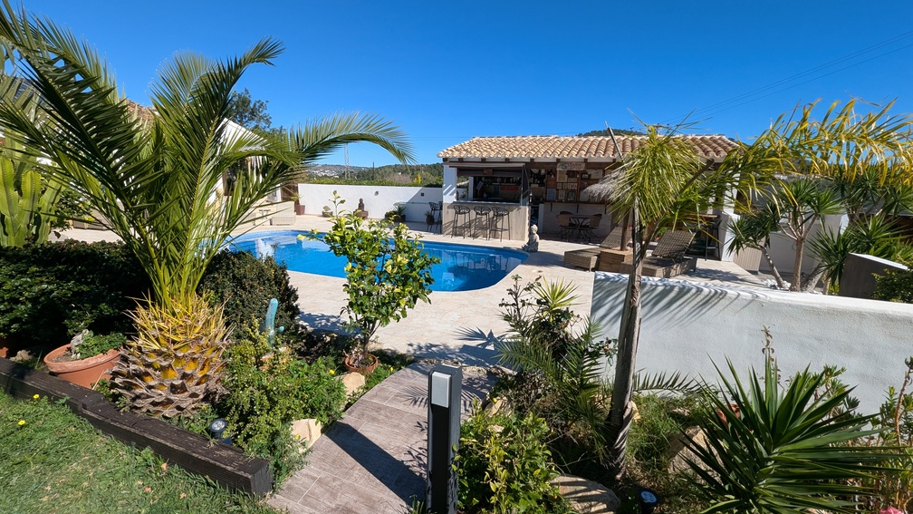 Outdoor pool area featuring a stone terrace, Mediterranean landscaping with palm trees, and a fully equipped covered summer kitchen with a bar.