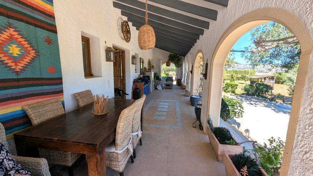 Traditional Mediterranean naya featuring arched openings, exposed ceiling beams, and a dining area with wicker seating overlooking the garden.