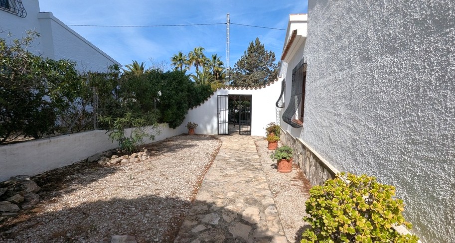 A stone-paved pathway leads through a gravel courtyard, bordered by whitewashed walls with traditional stone accents and wrought-iron window grilles.