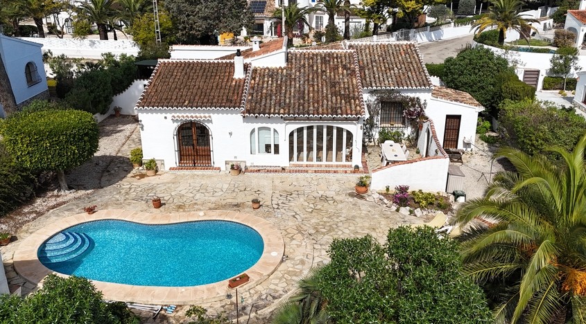 Aerial view of the traditional villa featuring a kidney-shaped pool, expansive stone terrace, and classic Mediterranean architecture with terracotta roof tiles.