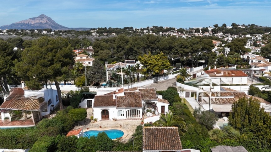 Aerial view of the traditional villa featuring a private pool, terracotta roofing, and a lush garden with the Montgó mountain in the background.