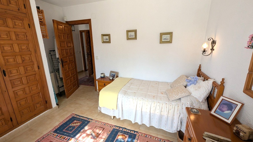 Bedroom featuring traditional built-in wooden wardrobes with carved panels, tiled flooring, and a single bed. The space includes rustic wooden doors and white textured walls.