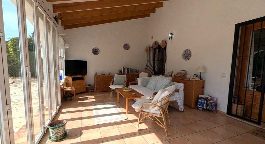 Bright enclosed naya featuring exposed wooden ceiling beams, terracotta flooring, and large glass sliding doors opening to the terrace.