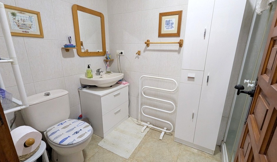 Functional bathroom featuring a white vanity unit, a wooden-framed mirror, and integrated storage cabinets. Includes a heated towel rack and tiled walls.