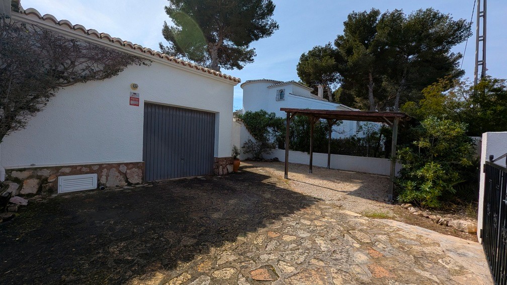Garage and wooden carport area with a stone-paved driveway and white facade featuring traditional stone accents.