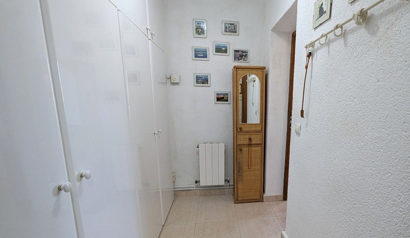 Hallway or dressing area featuring floor-to-ceiling white built-in wardrobes, a wicker storage unit with mirror, and a wall-mounted radiator.