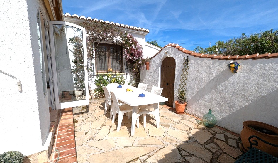 Private outdoor patio with irregular stone paving, a white dining set, and traditional Mediterranean architecture featuring arched doorways and terracotta tile accents.