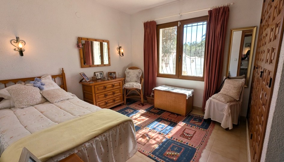 Traditional bedroom featuring built-in wooden wardrobes with decorative panels, a matching dresser, and natural light through a window with security bars.