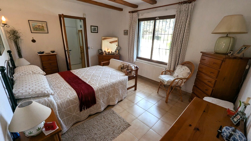 Traditional bedroom featuring exposed wooden ceiling beams, tiled flooring, and a radiator under the window providing natural light and comfort.
