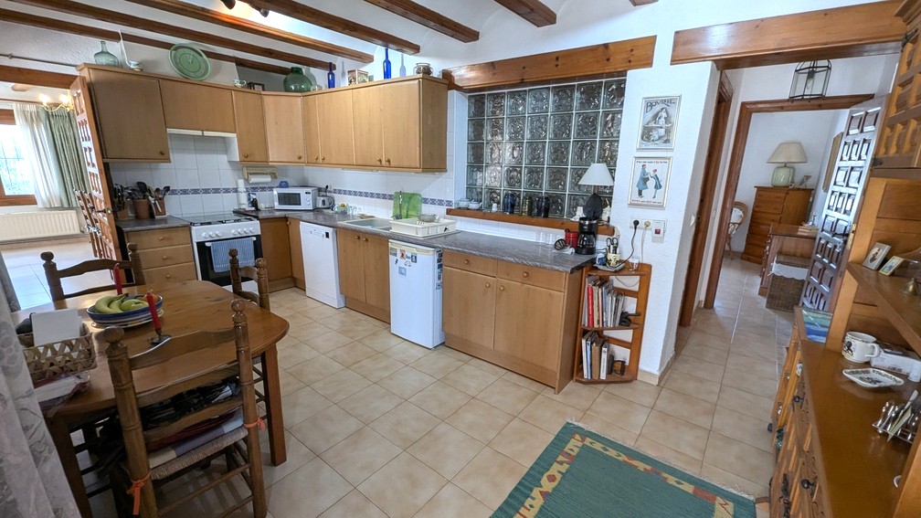 Traditional kitchen featuring exposed wooden ceiling beams, light wood cabinetry, and a glass block wall partition for natural light.
