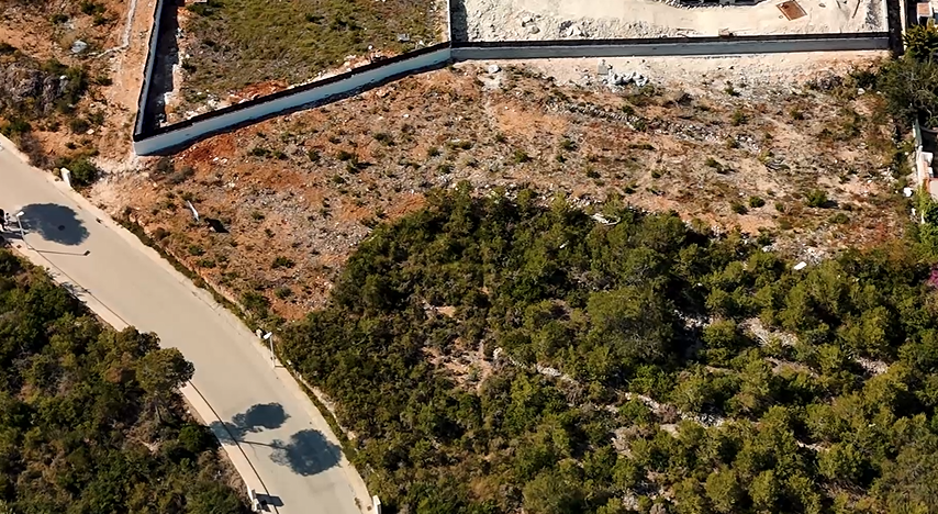 Aerial view of the 1,528 m² plot in Lomas del Rey, showing the excavated terrain, perimeter retaining wall, and direct access from the paved residential road.