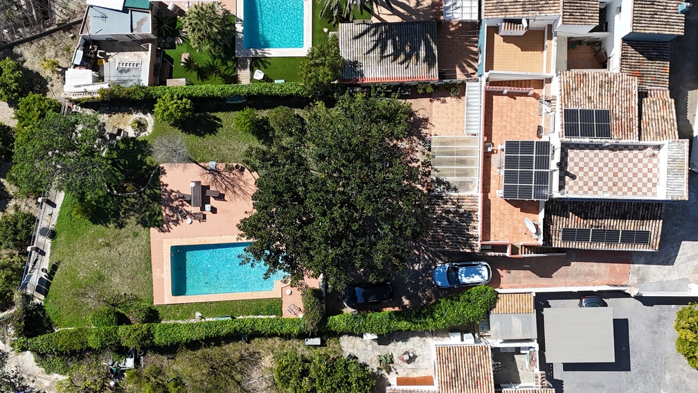 Aerial view of the villa featuring a private pool, lawn, and solar panels installed on the terracotta tiled roof, surrounded by lush Mediterranean greenery.