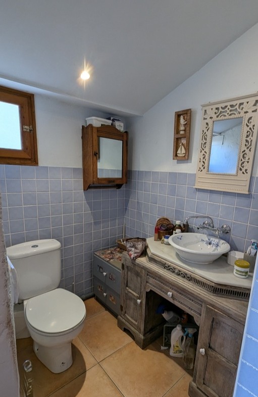 Bathroom featuring a rustic wooden vanity with a marble top, floral ceramic basin, and ornate mirrors set against light blue wall tiling and terracotta flooring.