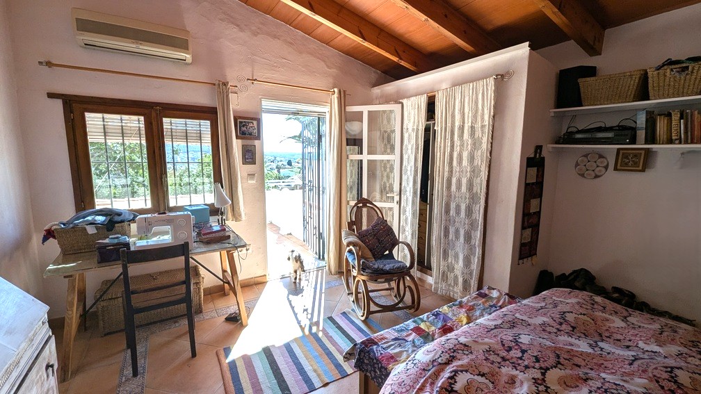 Bedroom featuring exposed wooden ceiling beams, terracotta flooring, and direct access to a terrace with countryside views. Includes a workspace and air conditioning.