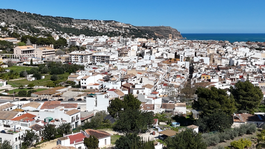 Elevated panoramic view of Javea Pueblo's historic center, showcasing traditional white-washed buildings, the San Bartolomé church tower, and the Mediterranean Sea.