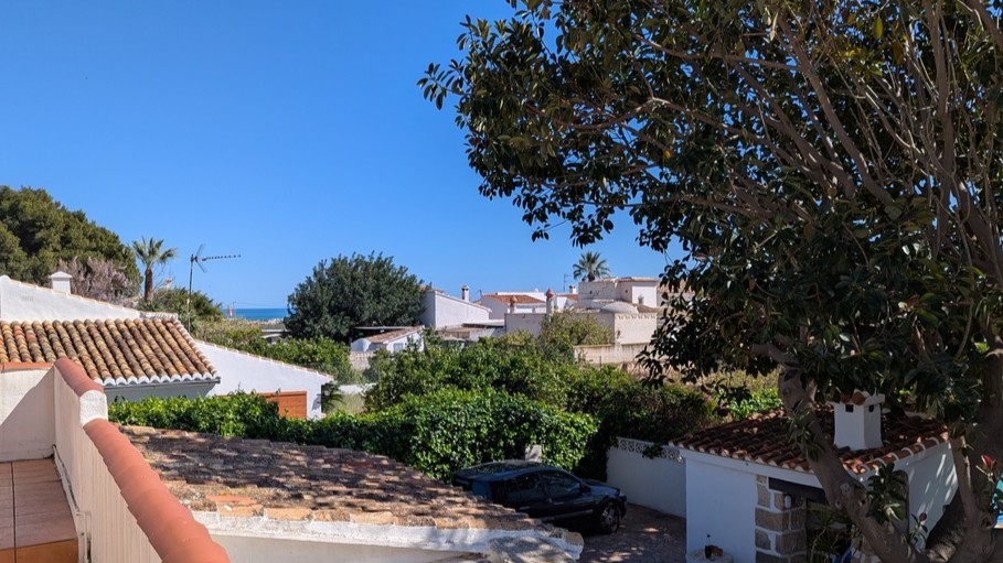 Elevated perspective from the upper terrace overlooking traditional tiled roofs, mature trees, and a distant view of the Mediterranean Sea.