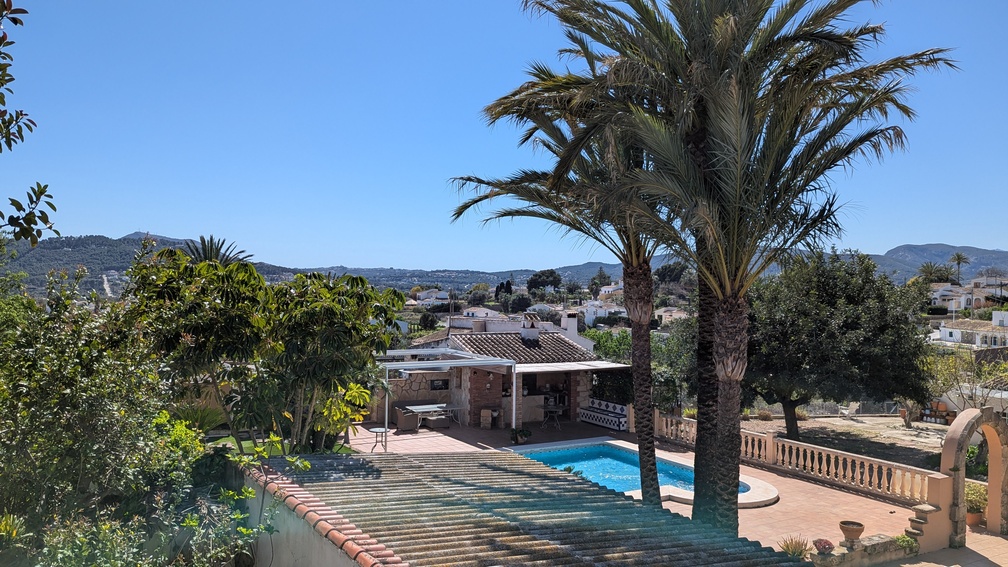 Elevated view of the private pool and terrace area, featuring a traditional outdoor kitchen, mature palm trees, and panoramic vistas of the Javea countryside.