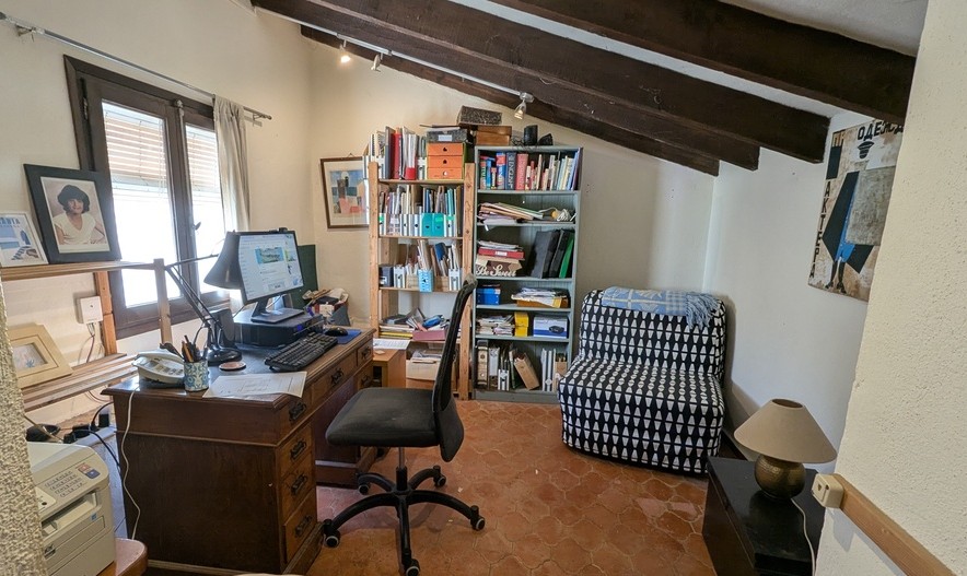 Home office featuring traditional terracotta flooring, exposed dark wood ceiling beams, a classic wooden desk, and natural light from a side window.