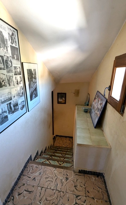 Interior staircase featuring traditional patterned floor tiles and decorative mosaic risers. A wooden-framed window provides natural light alongside framed artwork.