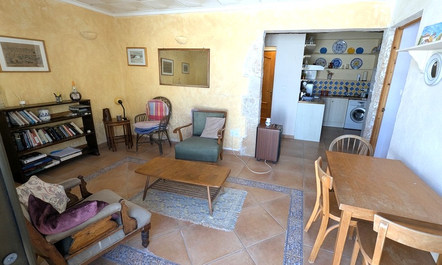 Living area of the guest apartment featuring terracotta floors with decorative borders, yellow textured walls, and a Tosca stone arch leading to the kitchenette.