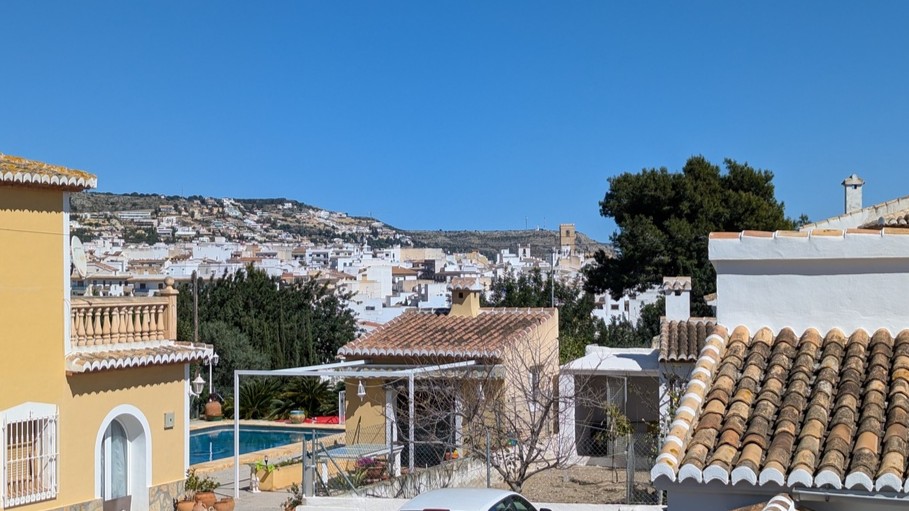 Panoramic view from the upper terrace overlooking Javea Pueblo's white architecture, terracotta rooftops, and a private swimming pool under a clear sky.
