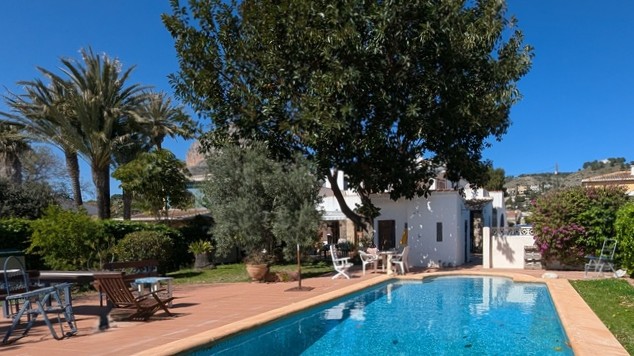 Private rectangular swimming pool with terracotta tiling, surrounded by a mature Mediterranean garden with palm trees and views of the Montgó mountain.