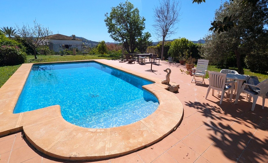 Private swimming pool with blue mosaic tiling, surrounded by a spacious terracotta terrace and a mature Mediterranean garden with open mountain views.