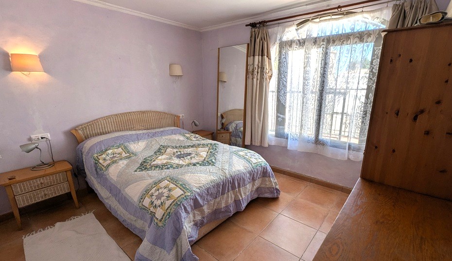 Spacious bedroom featuring lavender walls, traditional terracotta floor tiles, a wicker-accented bed, and a large window providing ample natural light.