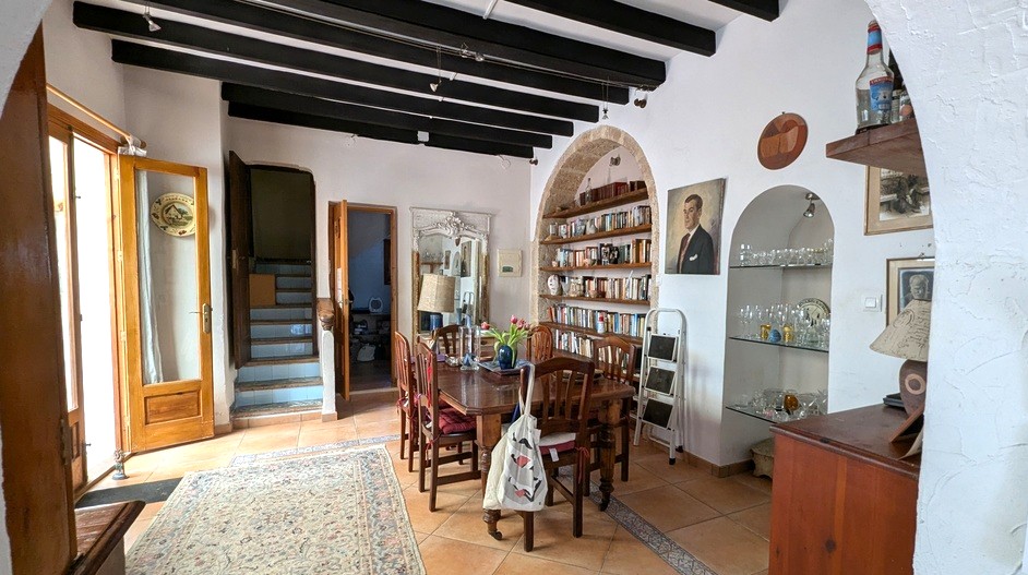 Spacious dining area featuring traditional dark wood ceiling beams, a Tosca stone arched bookshelf, and terracotta flooring leading to a tiled staircase.