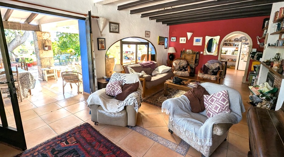 Spacious living room featuring dark wooden beams, terracotta tiling, and a red accent wall, opening directly onto a traditional south-facing naya.