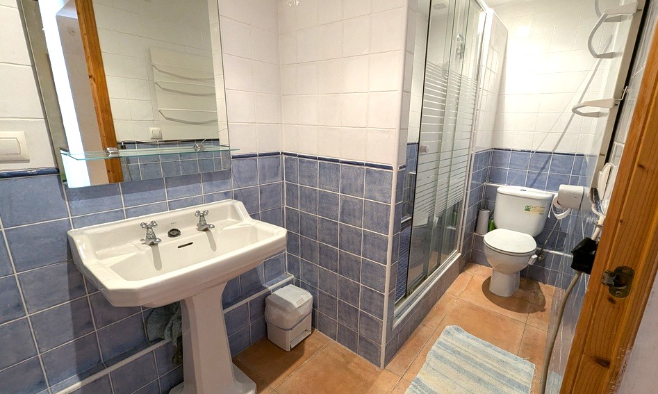 Traditional bathroom featuring blue and white wall tiles, a classic pedestal sink, terracotta flooring, and a walk-in shower with a glass enclosure.