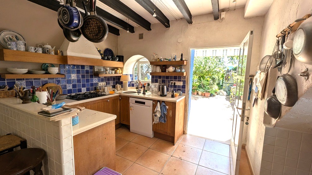 Traditional kitchen with dark wood ceiling beams, blue tiled backsplash, and wooden cabinetry, offering direct access to the sunlit garden terrace.
