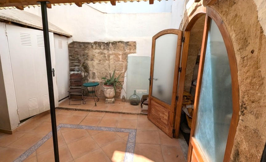 Traditional patio featuring exposed Tosca stone walls, terracotta tiling with decorative borders, and arched wooden doors leading to the interior.