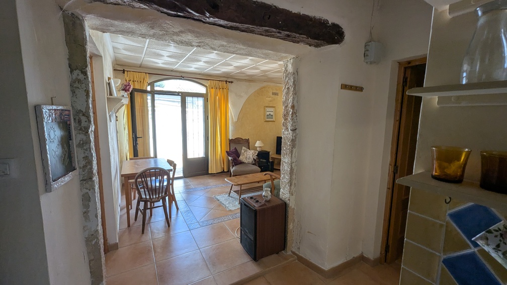 Traditional Tosca stone archway with a dark wooden beam leading to a bright living area with terracotta flooring and arched glass doors.