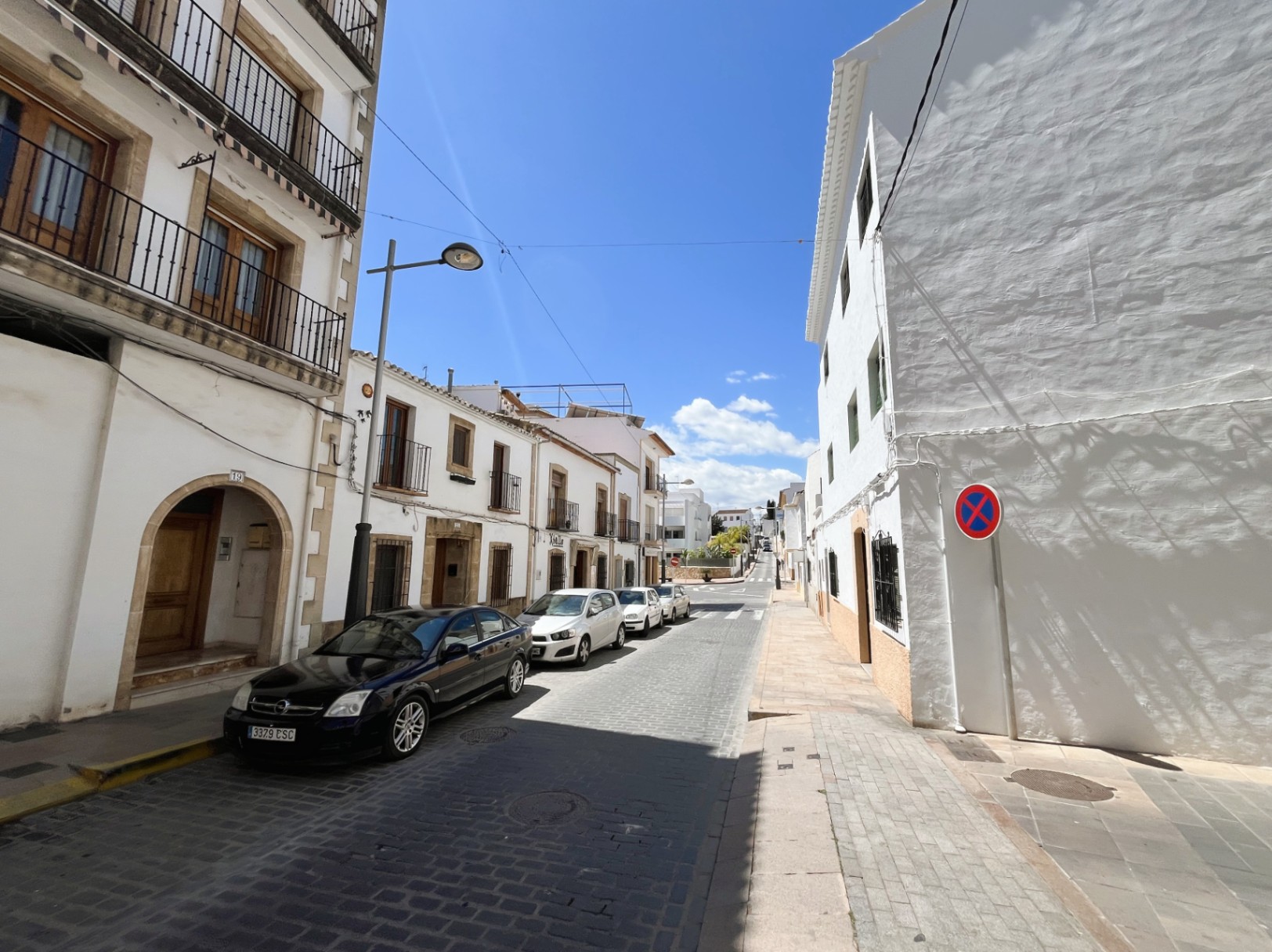 Exterior facade of the building located on a cobbled street in Jávea's old town, featuring traditional Tosca stone arches and wrought iron balconies.