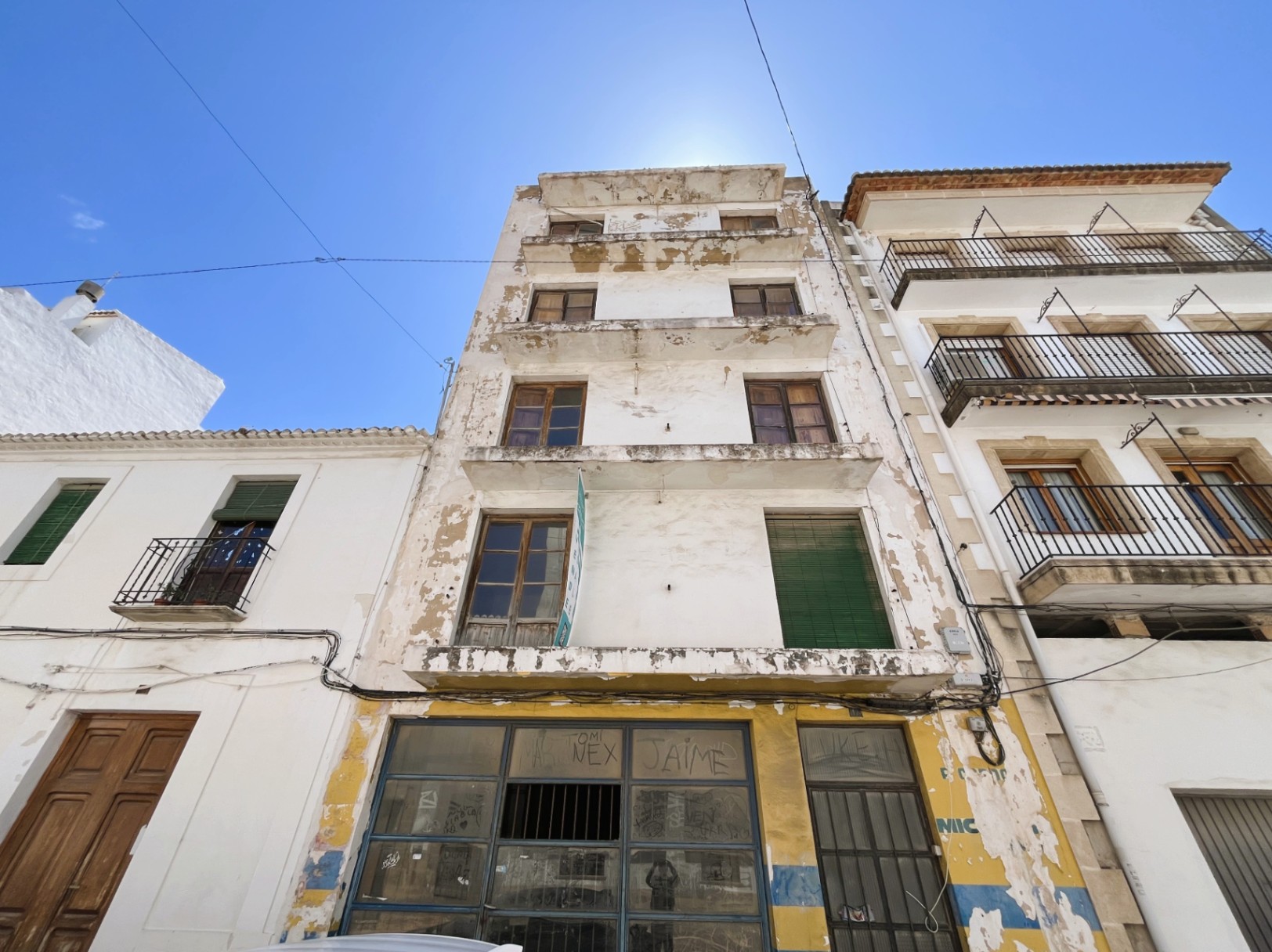 Four-story building facade featuring a ground-floor commercial space. The structure includes traditional wooden windows and balconies, ideal for a complete architectural renovation.