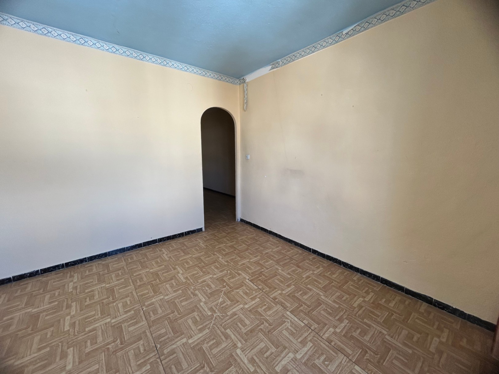 Interior room featuring patterned ceramic tile flooring, cream walls, and a light blue ceiling with decorative borders. An arched doorway connects to an adjacent space.