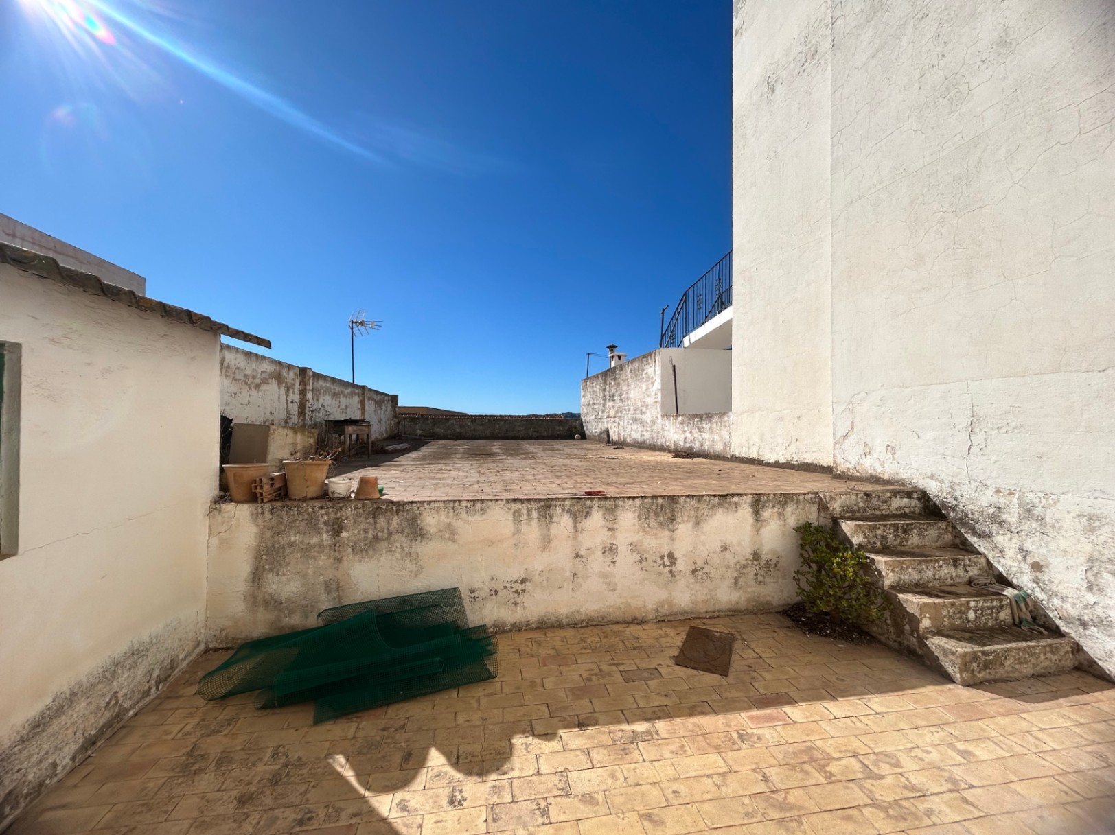 Multi-level rooftop terrace featuring tiled flooring and concrete stairs, offering an open outdoor space for renovation with clear sky views.