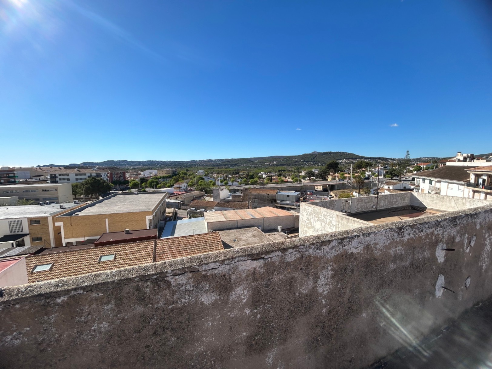 Panoramic views from the communal rooftop terrace overlooking the town of Jávea and the surrounding green hills under a clear, bright sky.